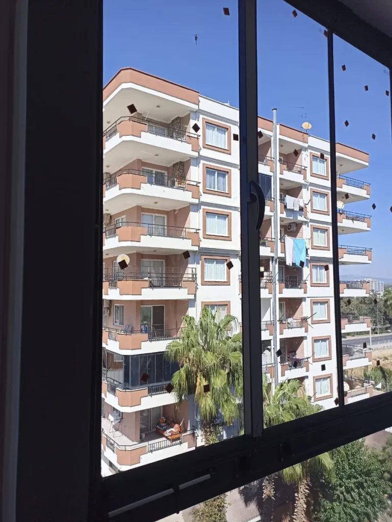 Siyah profilli cam balkonun içinden apartmanlar ve palmiye ağaçları görünümü