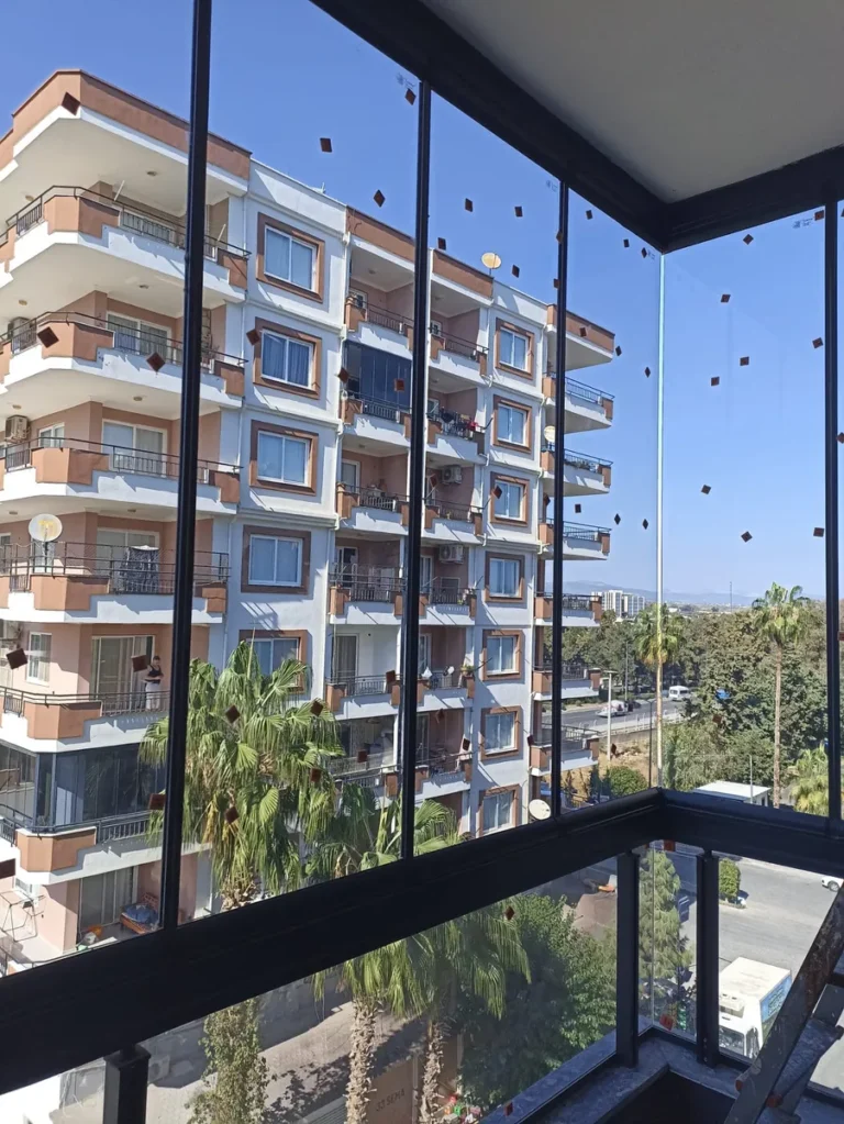 Siyah profilli cam balkon panelleri ve arkada apartman manzarası
